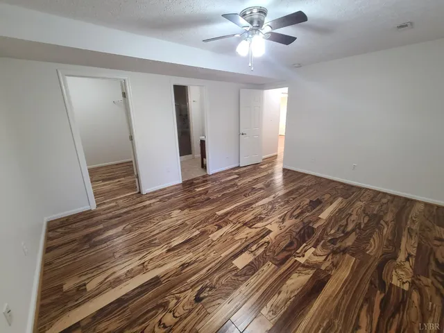 a view of an empty room with wooden floor and a ceiling fan