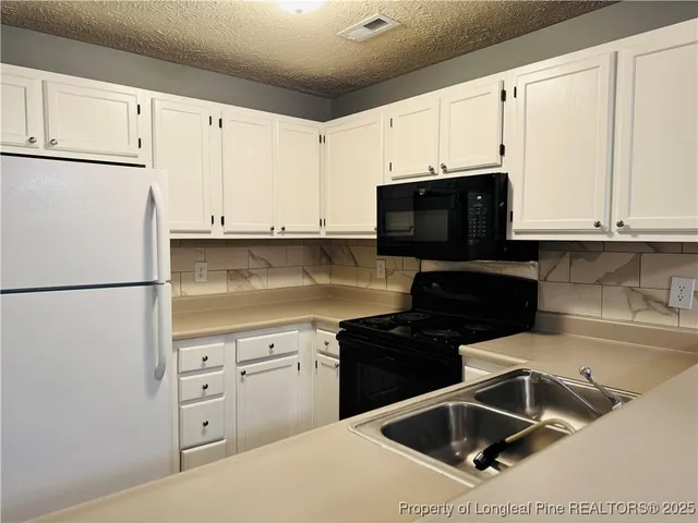 a kitchen with granite countertop a refrigerator sink and white cabinets