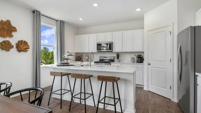 a kitchen with stainless steel appliances granite countertop a stove a refrigerator a sink and white cabinets with wooden floor