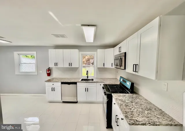 a kitchen with stainless steel appliances granite countertop a stove top oven a sink a refrigerator white cabinets and wooden floor