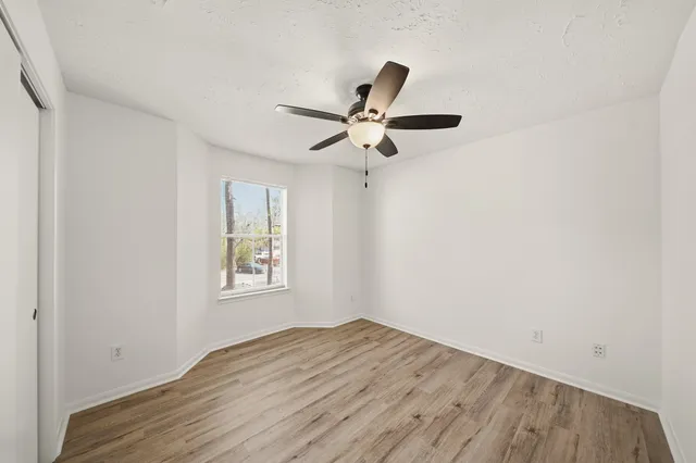 a view of empty room with wooden floor and fan