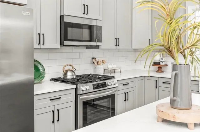 a kitchen with stainless steel appliances granite countertop a stove a sink dishwasher and white cabinets with wooden floor