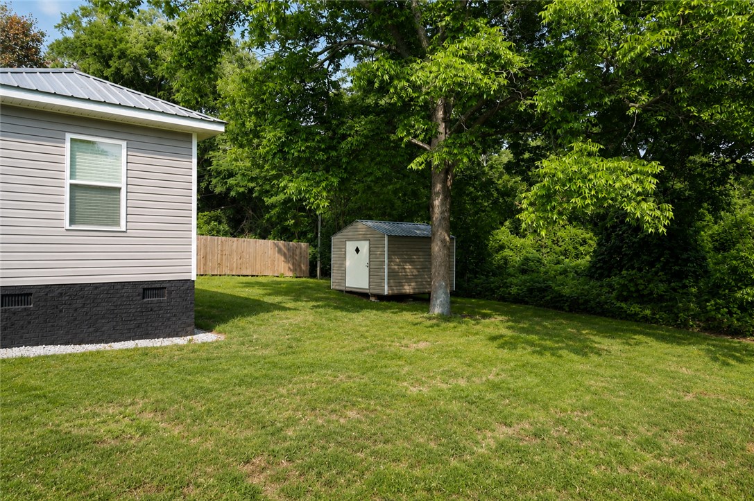 605 Hampton Street Iva, SC 29655 - Photo 15 of 16 A quaint storage shed nestled amidst lush greenery and mature trees in a verdant backyard.