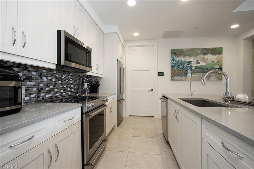 1035 3rd Avenue South, Unit 303 Naples, FL 34102 - Photo 7 of 26 a kitchen with stainless steel appliances granite countertop a sink and a stove top oven with wooden floor