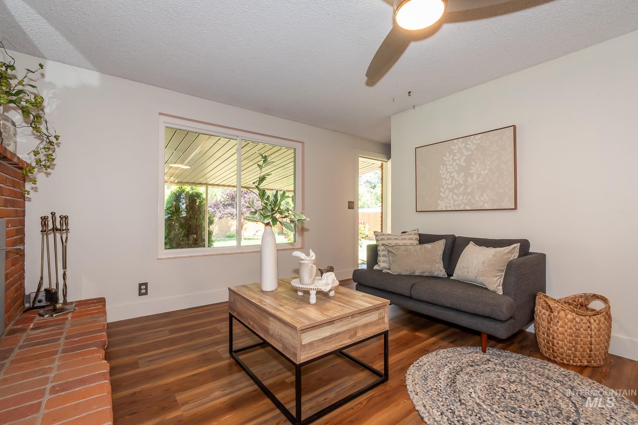 3706 West Clement Road Boise, ID 83704 - Photo 13 of 36 Bright, sun-filled living room showcasing rich wood-finish flooring, large picture windows with natural light, a ceiling fan with integrated lighting, and neutral wall finishes