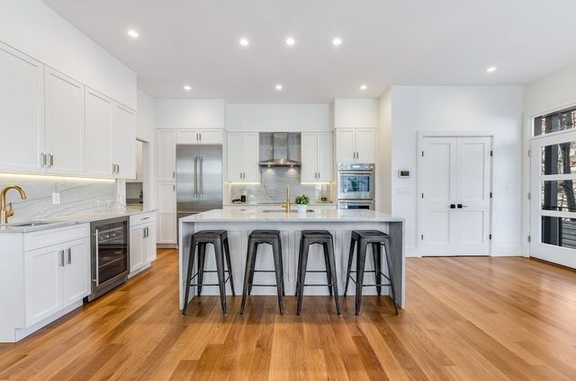 a kitchen with stainless steel appliances granite countertop a stove top oven a sink dishwasher a refrigerator and white cabinets with wooden floor