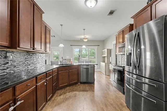 a kitchen with stainless steel appliances granite countertop a refrigerator a sink dishwasher a stove and a refrigerator with wooden floor