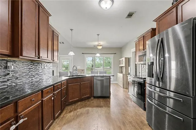 a kitchen with stainless steel appliances granite countertop a refrigerator a sink dishwasher a stove and a refrigerator with wooden floor