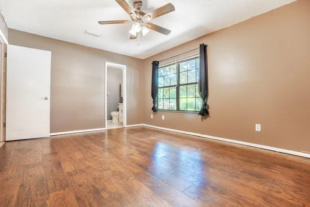 an empty room with wooden floor chandelier fan and windows