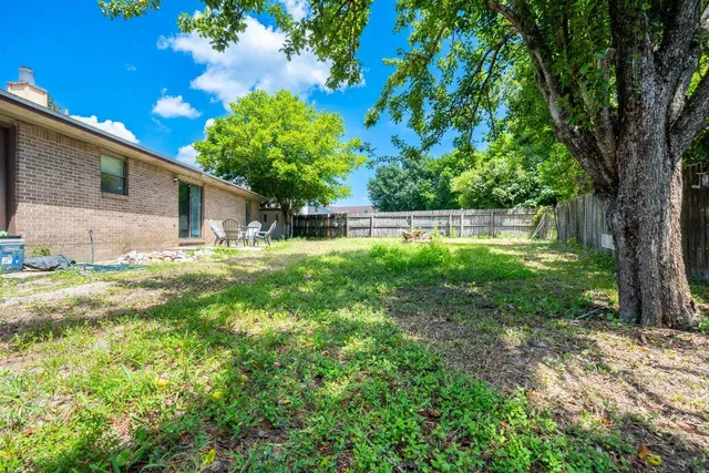 a backyard of a house with table and chairs plants and large tree