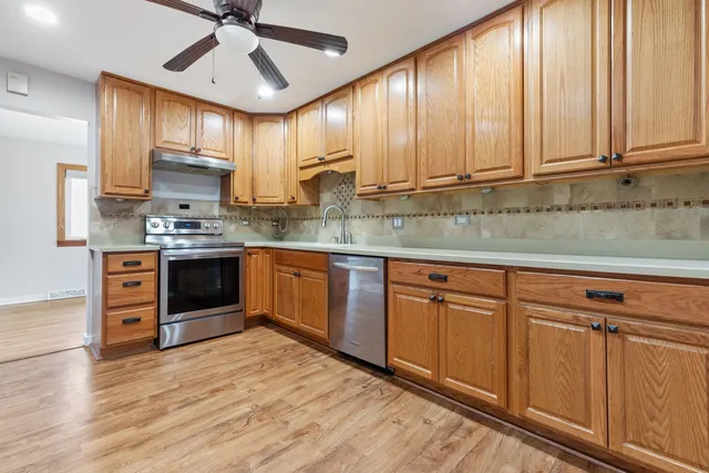 a kitchen with stainless steel appliances granite countertop wooden cabinets a sink a stove a refrigerator and island with wooden floor