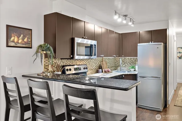 a kitchen with stainless steel appliances granite countertop a dining table chairs refrigerator and microwave