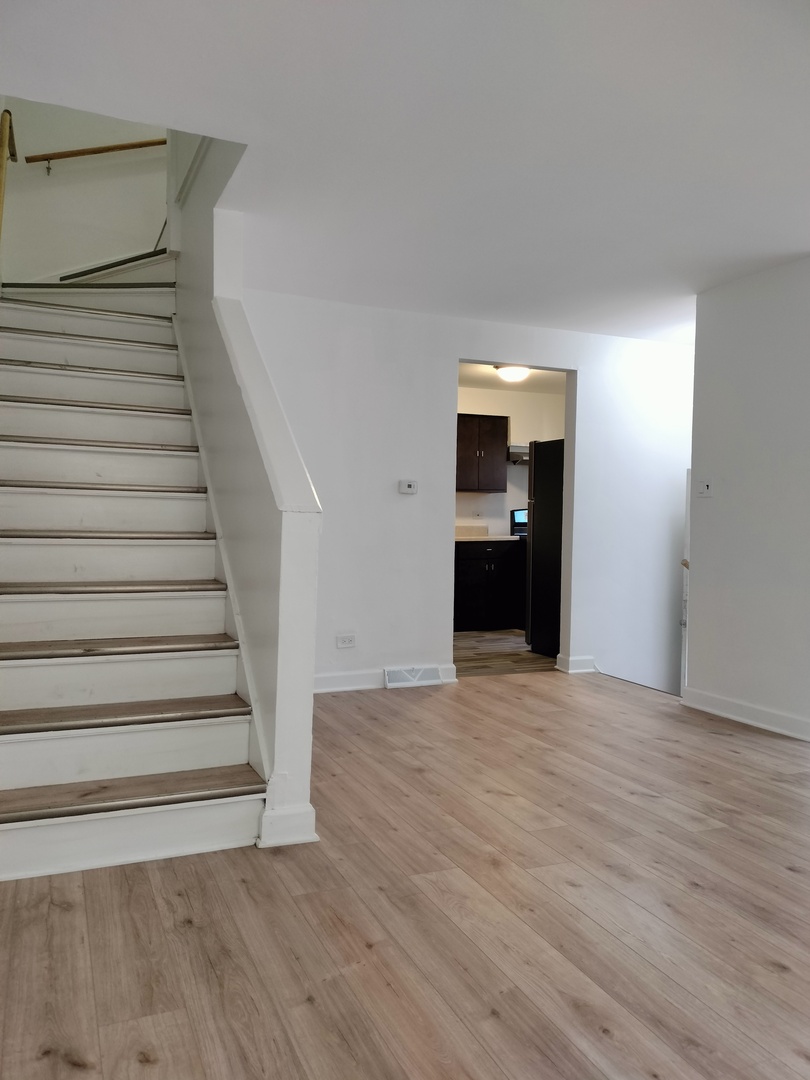 7910 South Muskegon Avenue, Unit 1 Chicago, IL 60617 - Photo 17 of 21 a view of an empty room with wooden floor and kitchen view