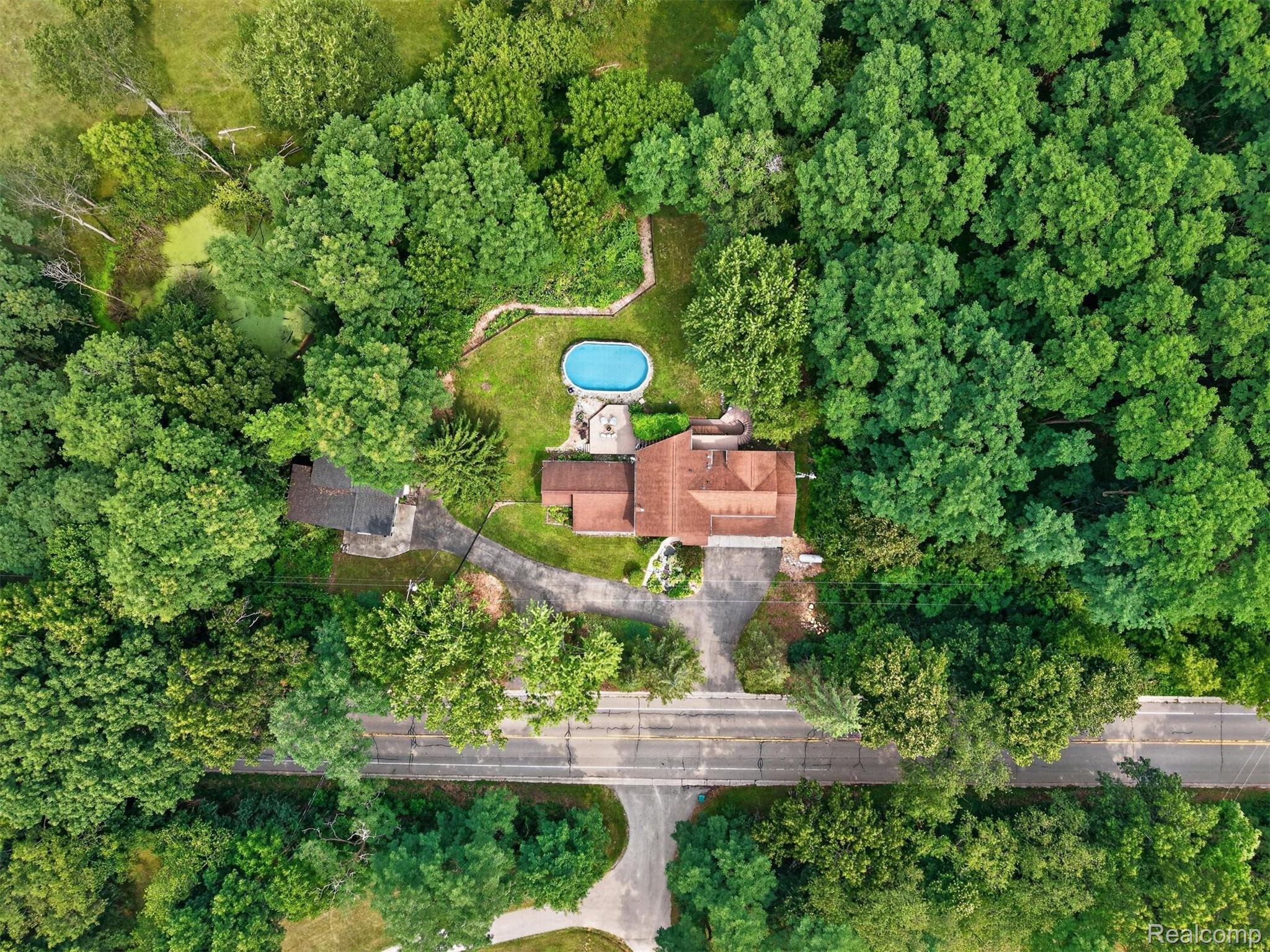 9319 Faussett Road Fenton, MI 48430 - Photo 62 of 70 Expansive wooded property featuring a main residence with a terracotta-colored roof, an additional outbuilding, a circular driveway, and a backyard swimming pool