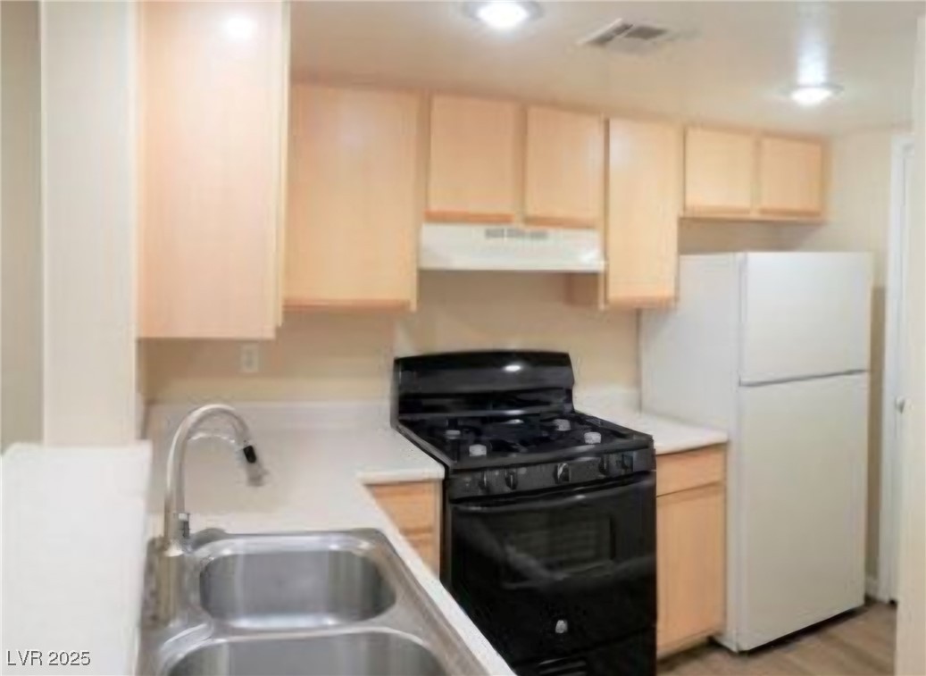 1830 North Pecos Road, Unit 131 Las Vegas, NV 89115 - Photo 8 of 13 Kitchen with a sink, extractor fan, light brown cabinetry, black gas range oven, and freestanding refrigerator