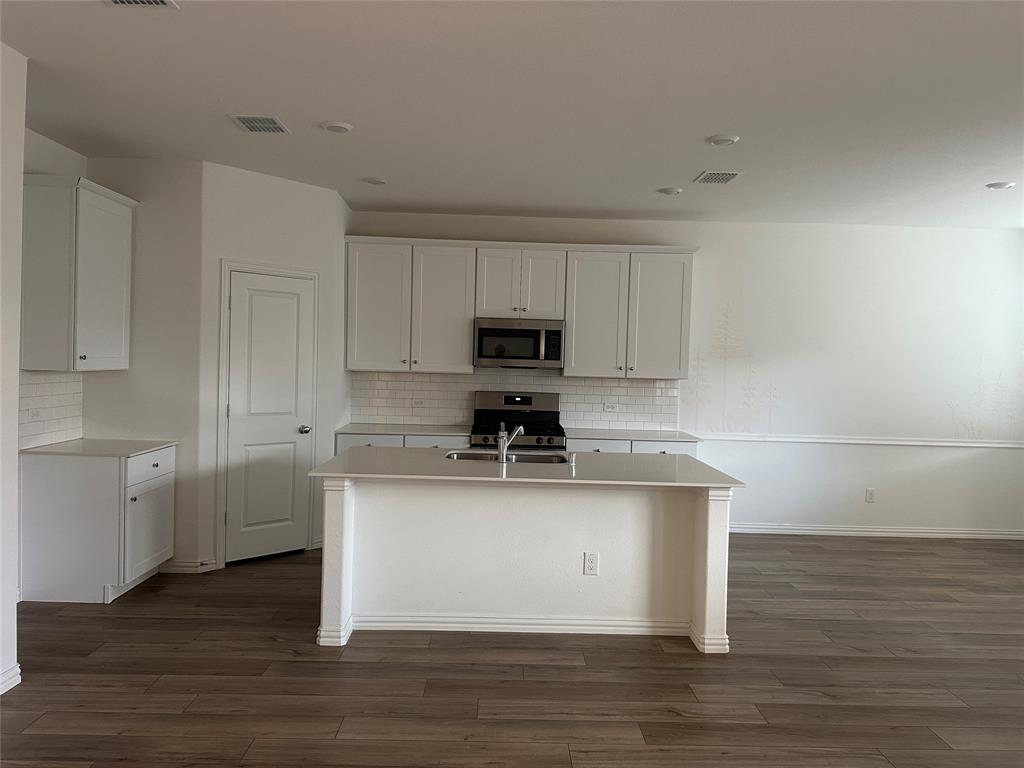 1462 Everett Gdns Way Forney, TX 75126 - Photo 4 of 14 Kitchen with white cabinetry, stainless steel appliances, a center island with sink, tasteful backsplash, and dark wood-type flooring