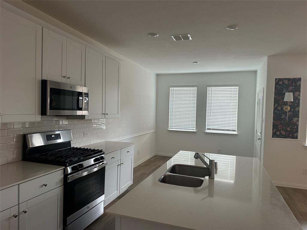 1462 Everett Gdns Way Forney, TX 75126 - Photo 5 of 14 Kitchen featuring stainless steel appliances, white cabinetry, dark wood-style flooring, and backsplash