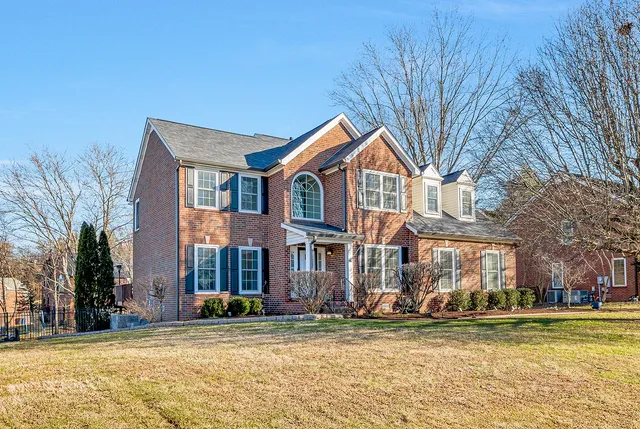 a view of a brick house with a big yard and large trees