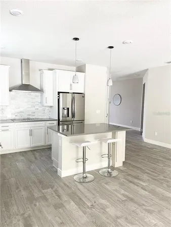 a kitchen with stainless steel appliances kitchen island granite countertop a refrigerator a stove and white cabinets with wooden floor