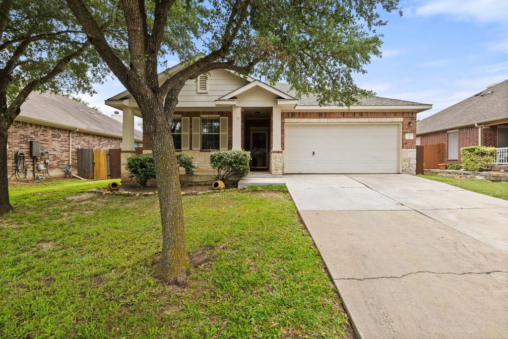 A welcoming front exterior showcasing a blend of brick and stone with mature trees framing the entry.