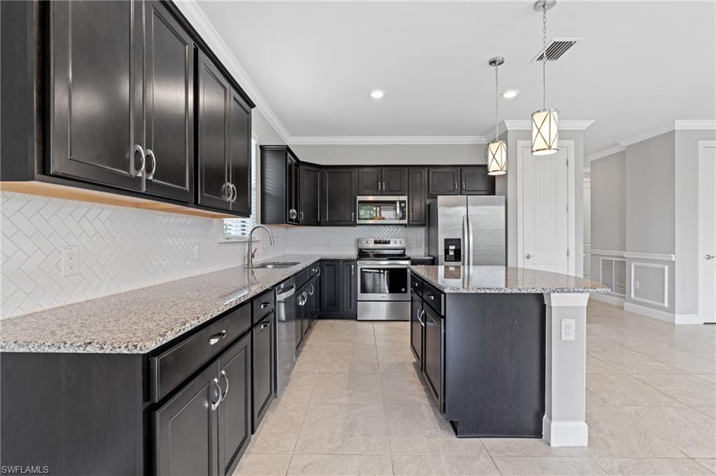 19953 Beverly Park Road Estero, FL 33928 - Photo 8 of 50 Kitchen with light stone countertops, ornamental molding, a sink, appliances with stainless steel finishes, and decorative light fixtures