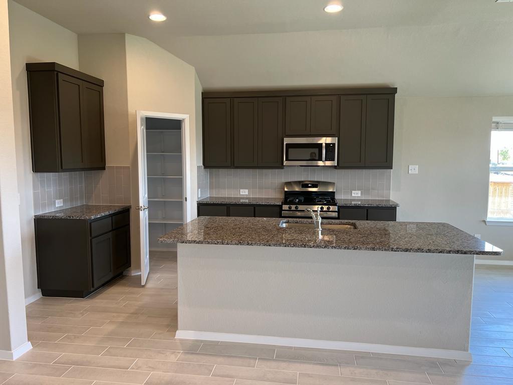 105 Spiny Lizard Lane San Marcos, TX 78666 - Photo 19 of 34 Kitchen with dark stone counters, wood tiled floors, appliances with stainless steel finishes, tasteful backsplash, and a center island with sink