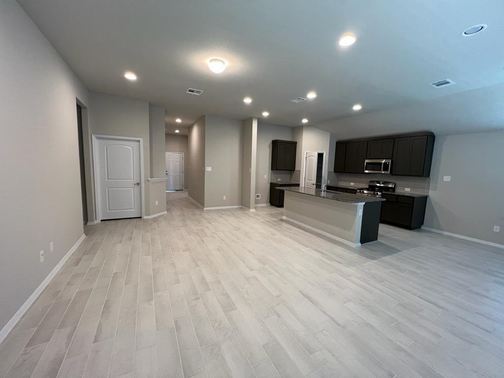 105 Spiny Lizard Lane San Marcos, TX 78666 - Photo 34 of 34 Kitchen featuring open floor plan, light wood finished floors, an island with sink, stainless steel microwave, and range with gas stovetop