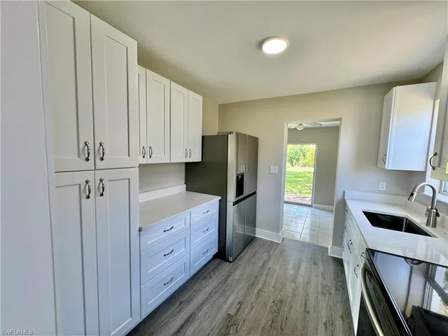 a kitchen with stainless steel appliances granite countertop a refrigerator a sink dishwasher and white cabinets with wooden floor