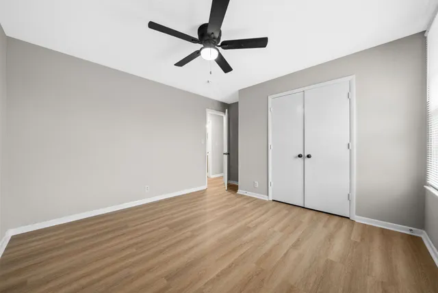 an empty room with wooden floor ceiling fan and windows