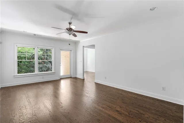 an empty room with wooden floor chandelier fan and windows