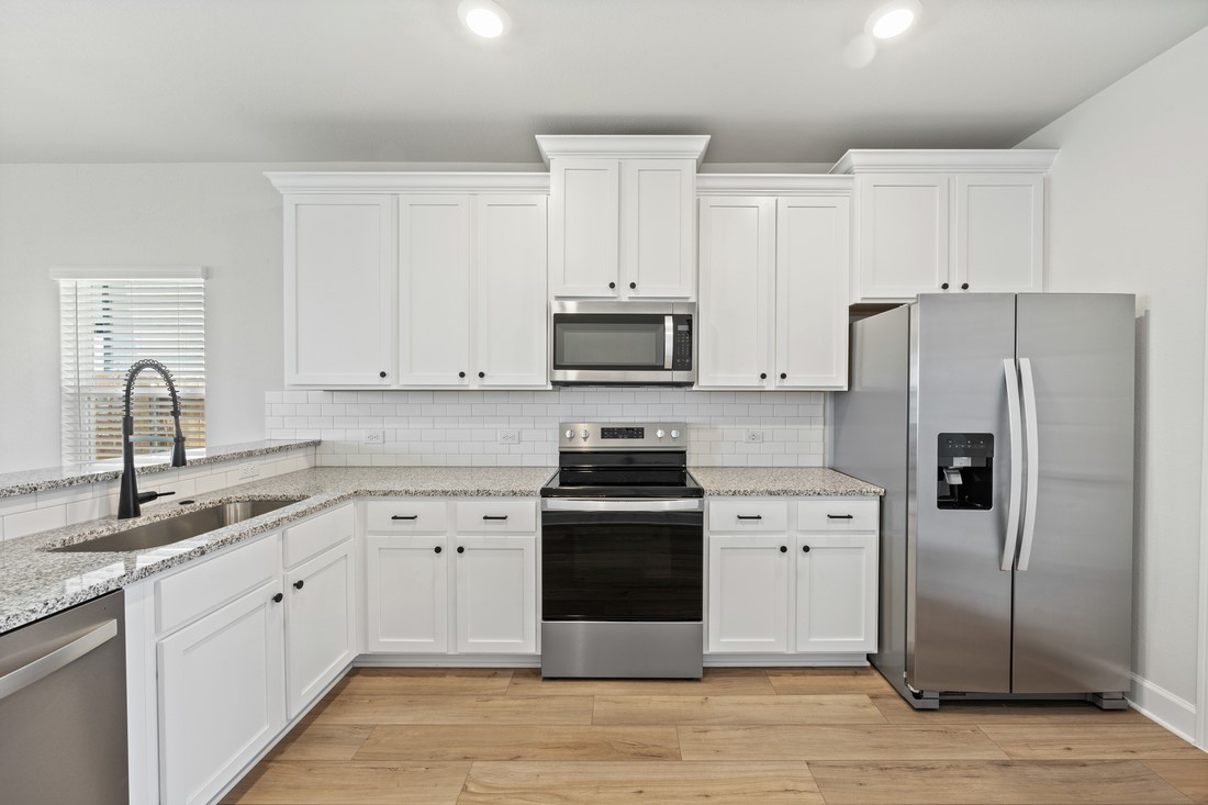 9316 Gladsome Path Manor, TX 78653 - Photo 7 of 18 a kitchen with white cabinets and stainless steel appliances