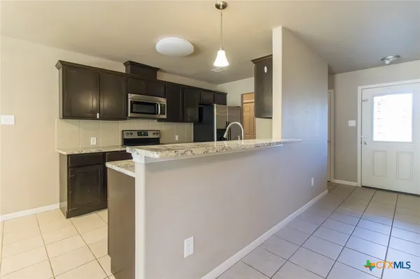 an empty room with kitchen view and a chandelier fan