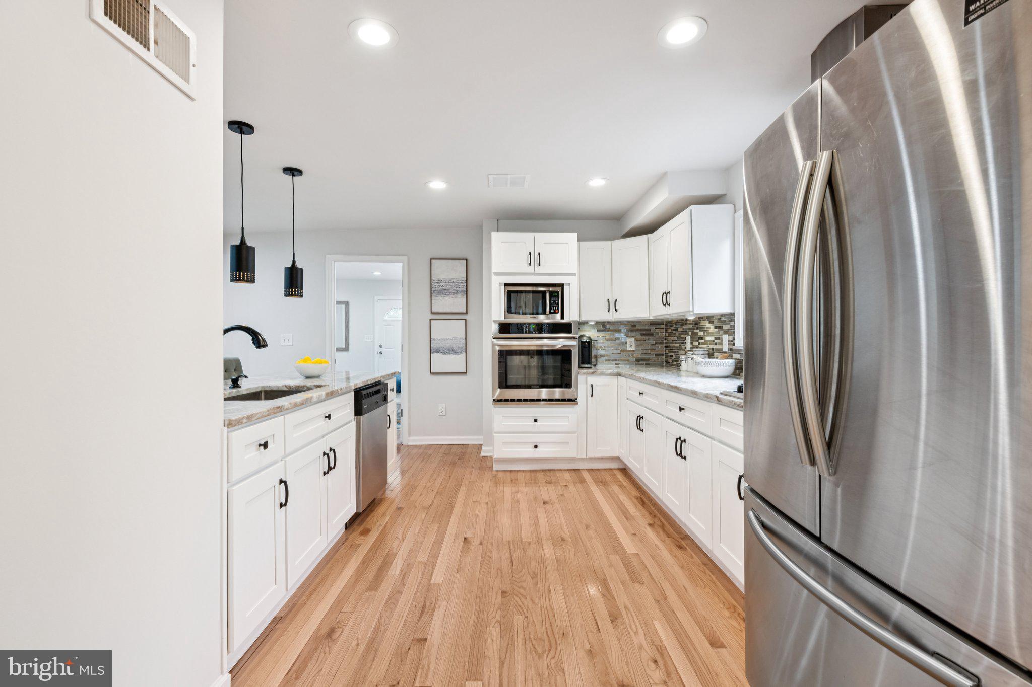 4014 37th Street Mount Rainier, MD 20712 - Photo 4 of 26 a large kitchen with stainless steel appliances granite countertop a refrigerator oven a sink dishwasher and white cabinets with wooden floor