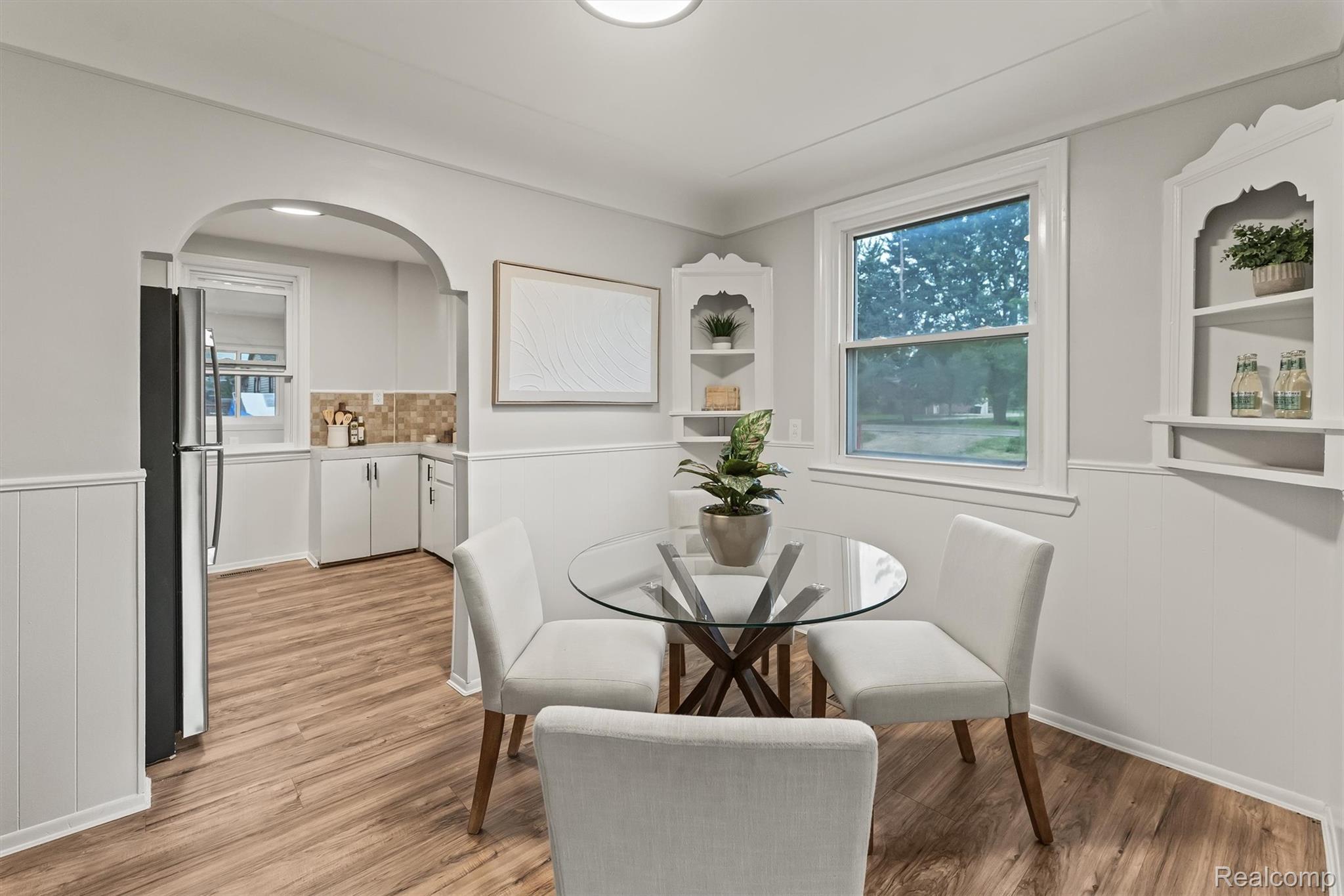 Wood-finish flooring throughout, archway entry, stainless steel refrigerator, white wainscoting, and built-in shelving