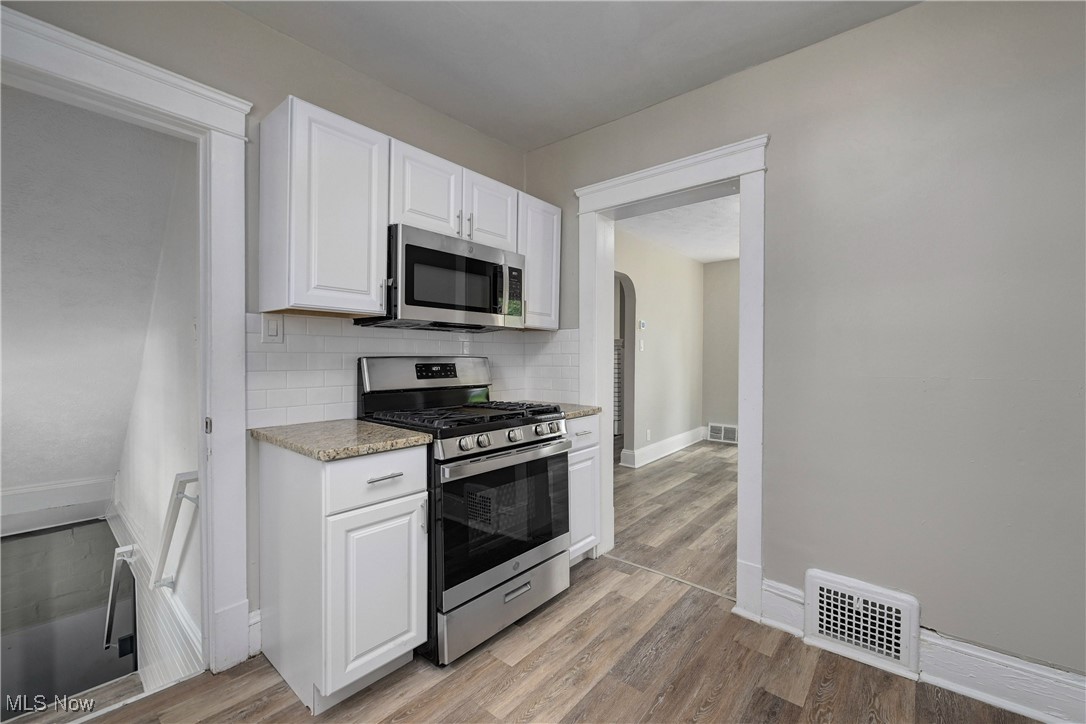 896 Selwyn Road Cleveland Heights, OH 44112 - Photo 9 of 23 Kitchen with stainless steel appliances, light wood-style floors, white cabinetry, backsplash, and arched walkways