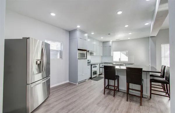 a kitchen with stainless steel appliances a refrigerator a stove a sink a dining table and chairs with wooden floor