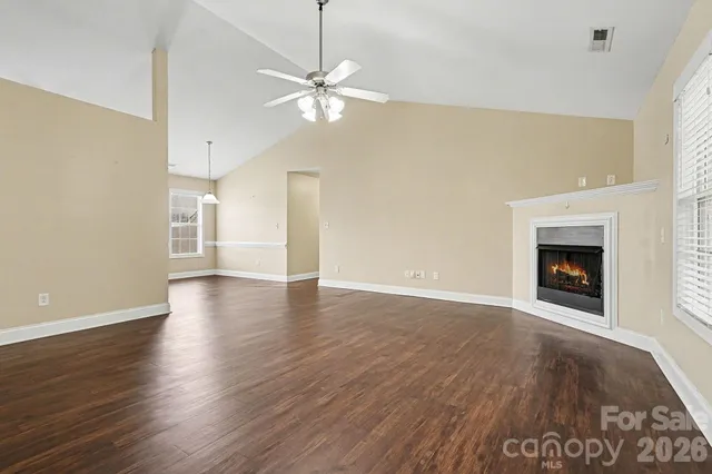 a view of an empty room with wooden floor fireplace and a window