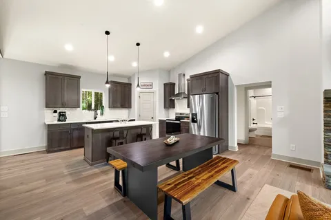 a kitchen with stainless steel appliances kitchen island granite countertop a refrigerator a stove a sink dishwasher and white cabinets with wooden floor