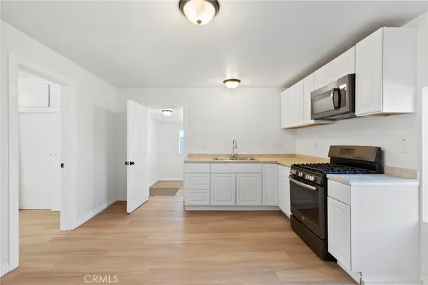 a kitchen with stainless steel appliances granite countertop a stove top oven a sink dishwasher and white cabinets with wooden floor