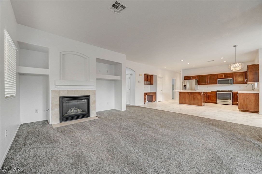 6012 Prospector Trail Las Vegas, NV 89118 - Photo 14 of 73 Unfurnished living room with a tiled fireplace, built in features, light colored carpet, recessed lighting, and arched walkways