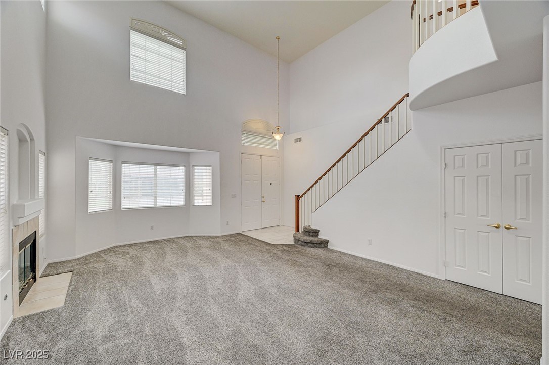 6012 Prospector Trail Las Vegas, NV 89118 - Photo 8 of 73 Unfurnished living room featuring a towering ceiling, a tile fireplace, carpet, and stairway