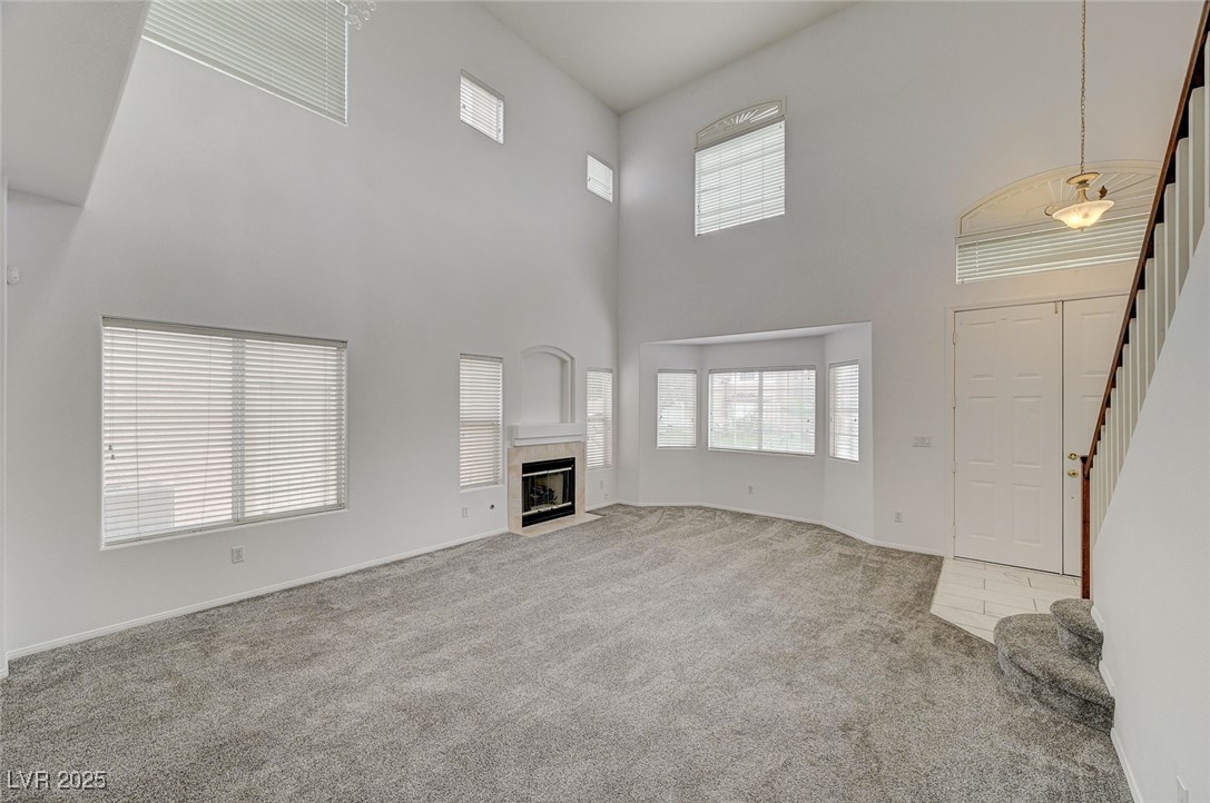 6012 Prospector Trail Las Vegas, NV 89118 - Photo 9 of 73 Unfurnished living room featuring stairway, light carpet, a high ceiling, and a tiled fireplace