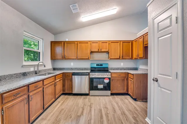 a kitchen with stainless steel appliances granite countertop wooden cabinets a sink a stove a refrigerator with grey cabinets and wooden floor