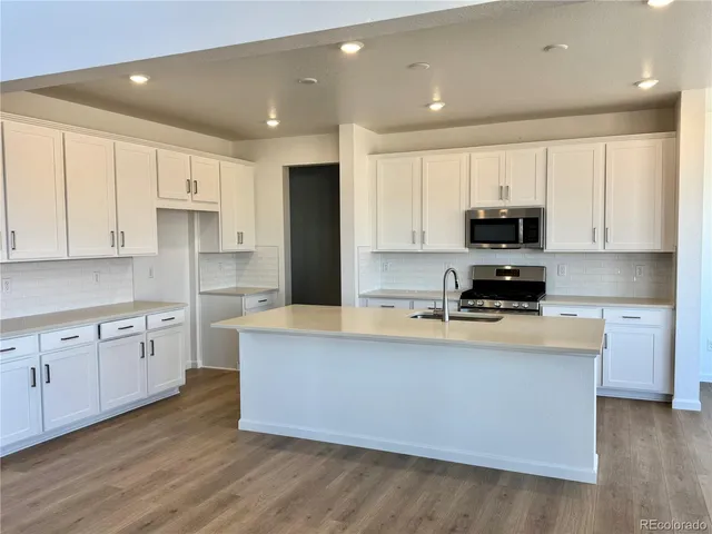 a large kitchen with stainless steel appliances granite countertop a stove a sink a refrigerator and white cabinets