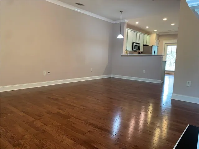 an empty room with wooden floor and kitchen view