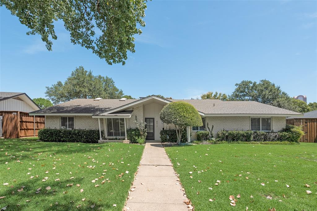 a view of house in front of a big yard with plants and large trees
