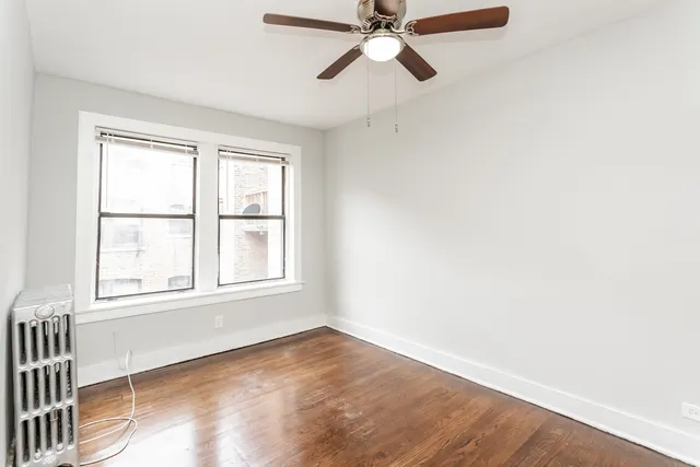 an empty room with wooden floor fan and windows