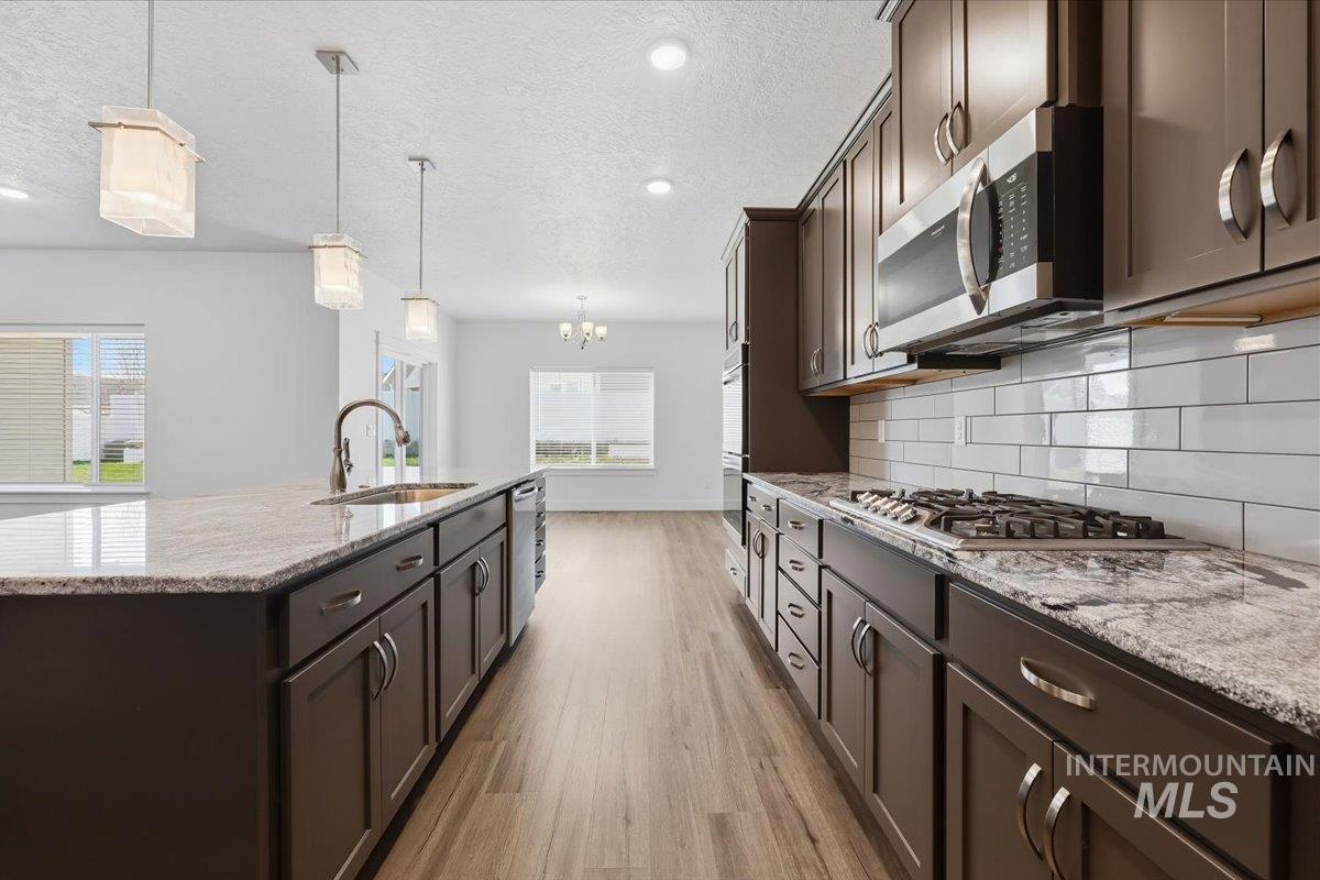 148 Homesteaders Street Middleton, ID 83644 - Photo 11 of 45 Kitchen featuring dark wood finish cabinets, light stone counters, an island with sink, light wood-style floors, and a textured ceiling