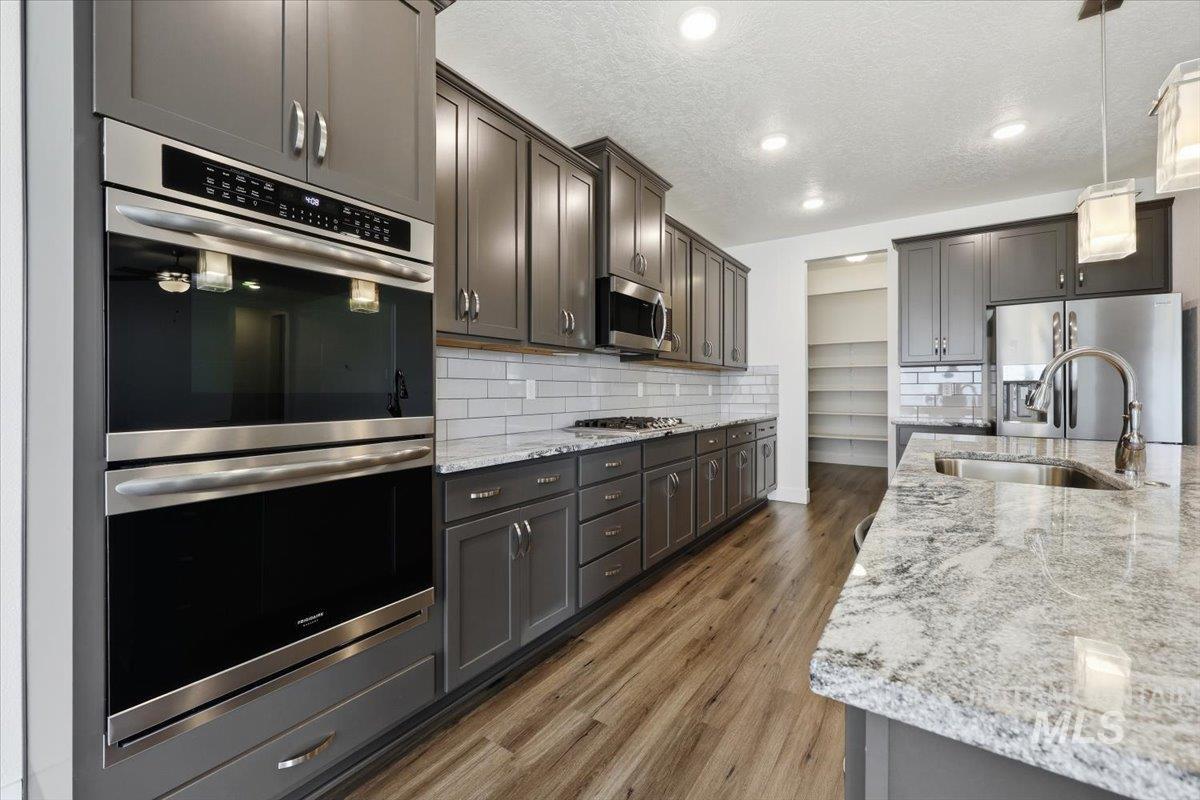 148 Homesteaders Street Middleton, ID 83644 - Photo 12 of 45 Kitchen with stainless steel appliances, light stone counters, dark wood-style flooring, hanging light fixtures, and backsplash