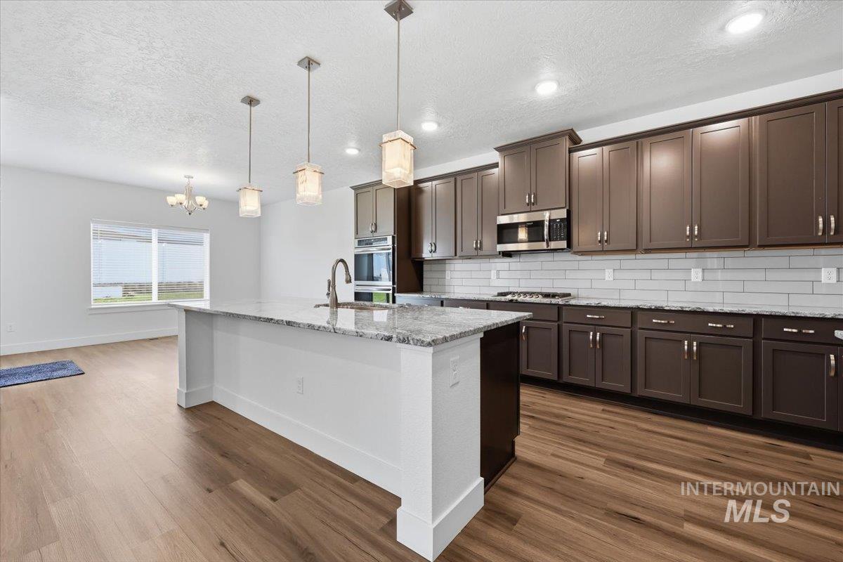 148 Homesteaders Street Middleton, ID 83644 - Photo 9 of 45 Kitchen with light stone counters, dark wood finish cabinets, tasteful backsplash, a textured ceiling, and a center island with sink